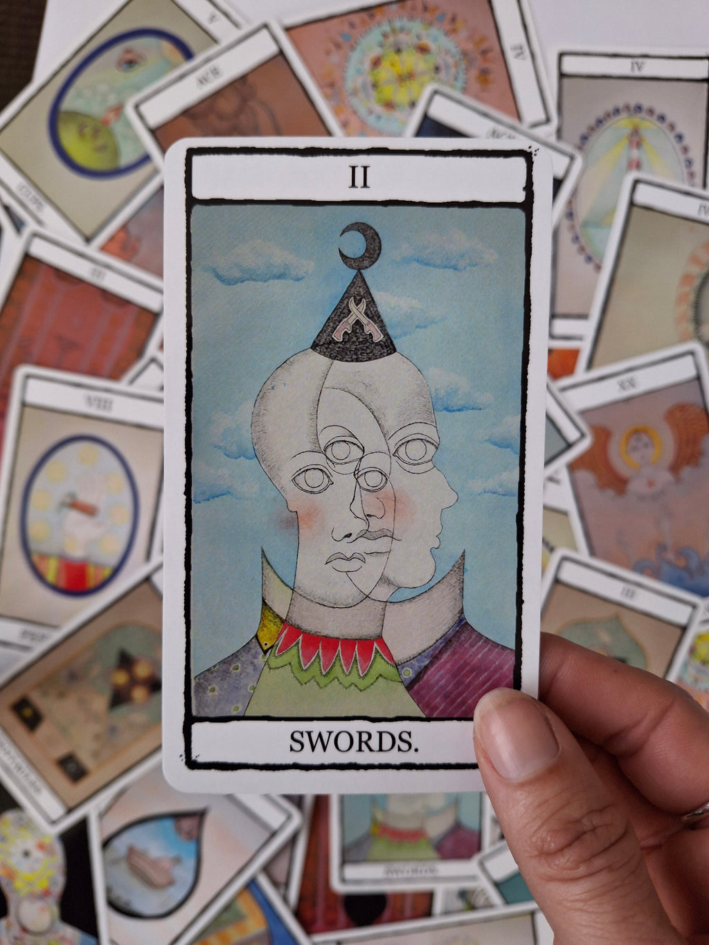 Colourful, surreal hand illustrated Two of Swords tarot card featuring two faces with brightly coloured costumes
