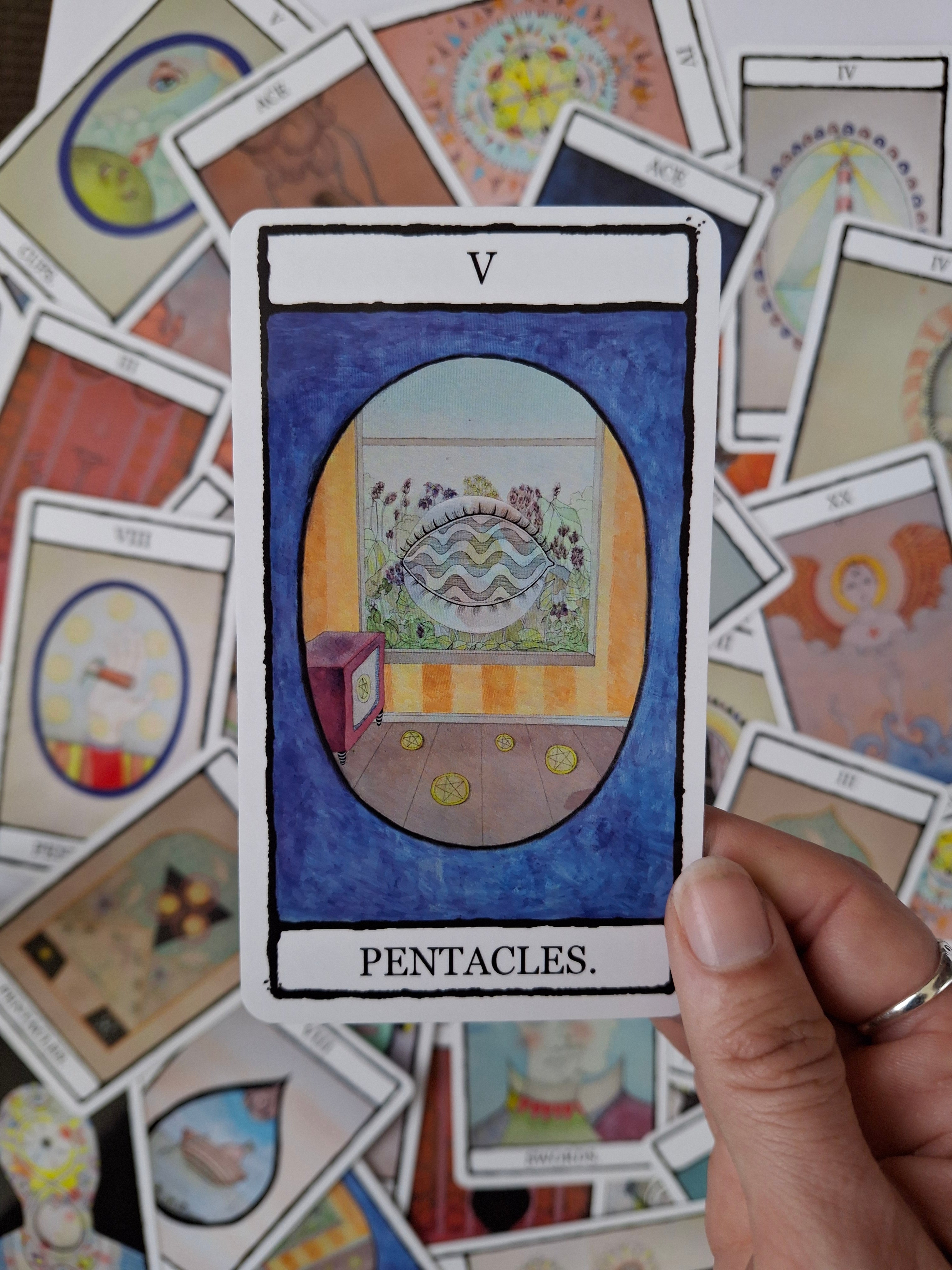 Tarot card with 5 of Pentacles illustration with a blue background and whimsical room with a surreal eye