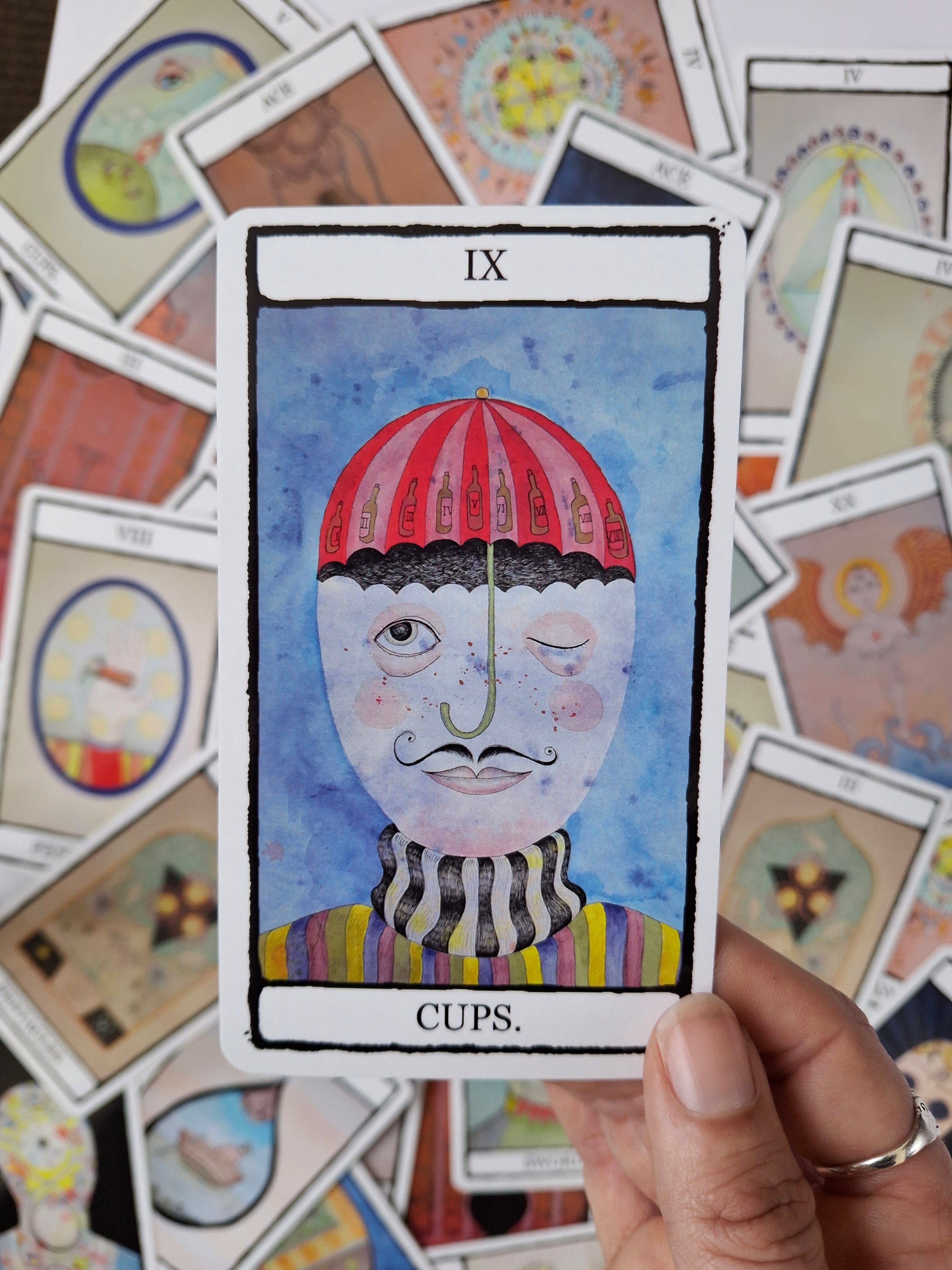 Hand illustrated Nine of Cups tarot card featuring a cute sailor with a red umbrella hat and rainbow striped costume