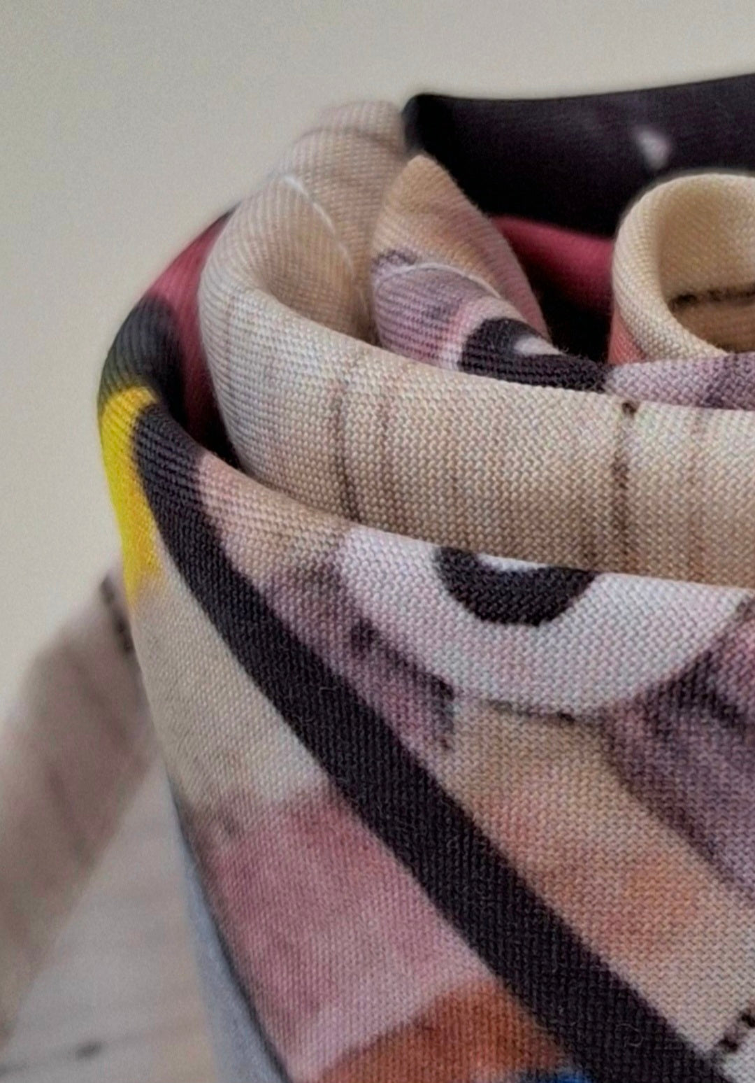 Close up of a printed scarf featuring original black, purple and yellow art