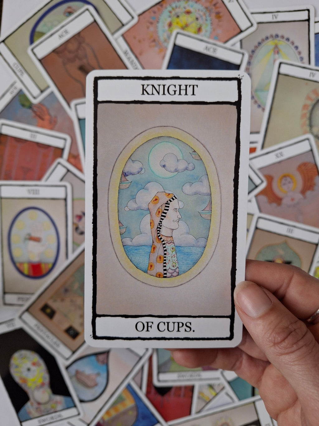 Tarot Card with 'Knight of Cups' illustration wearing intricately designed costume and blue sky with ships.
