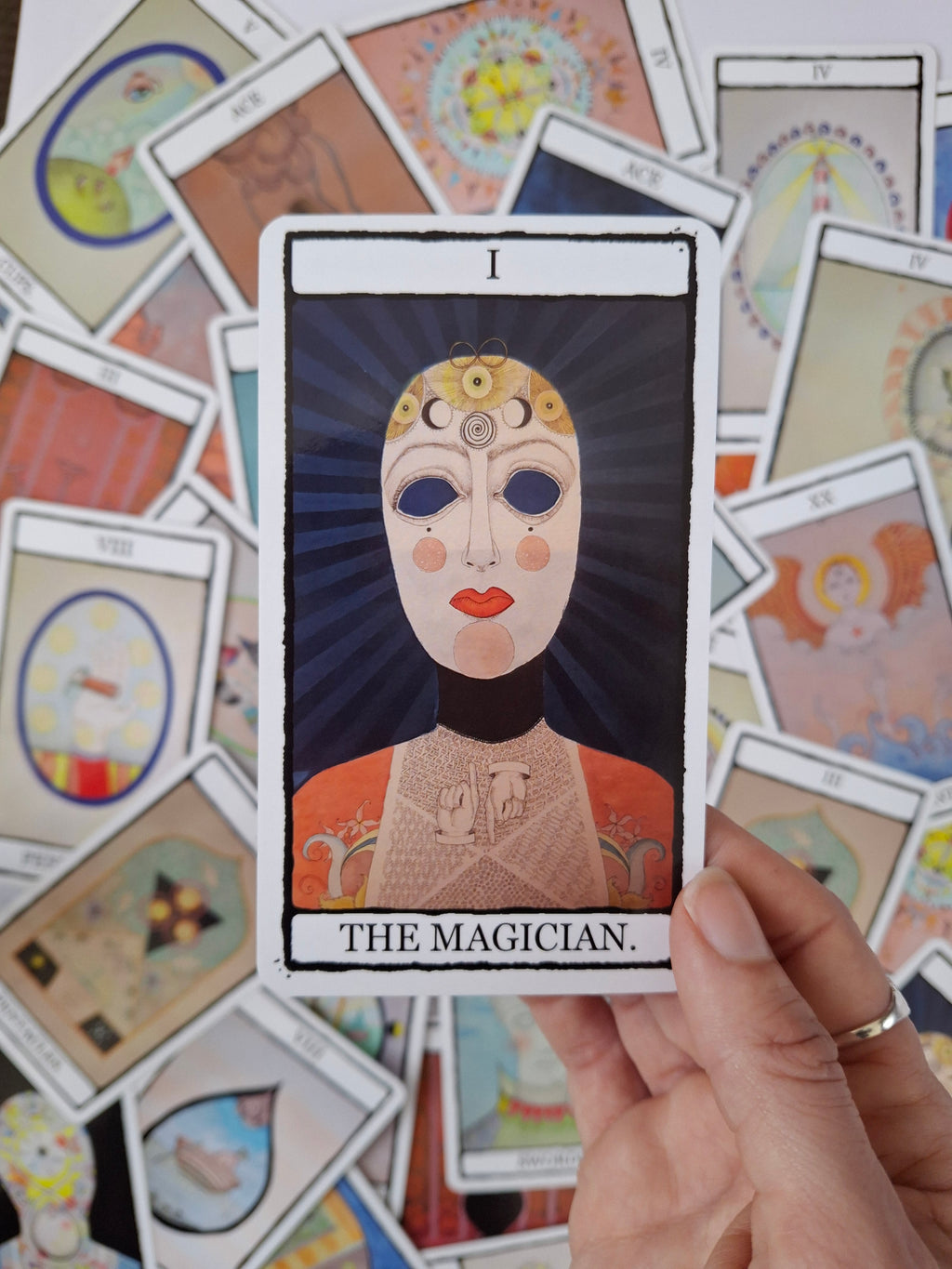 Tarot card 'The Magician' wearing an intricately designed costume, held above a scattered deck of tarot cards.