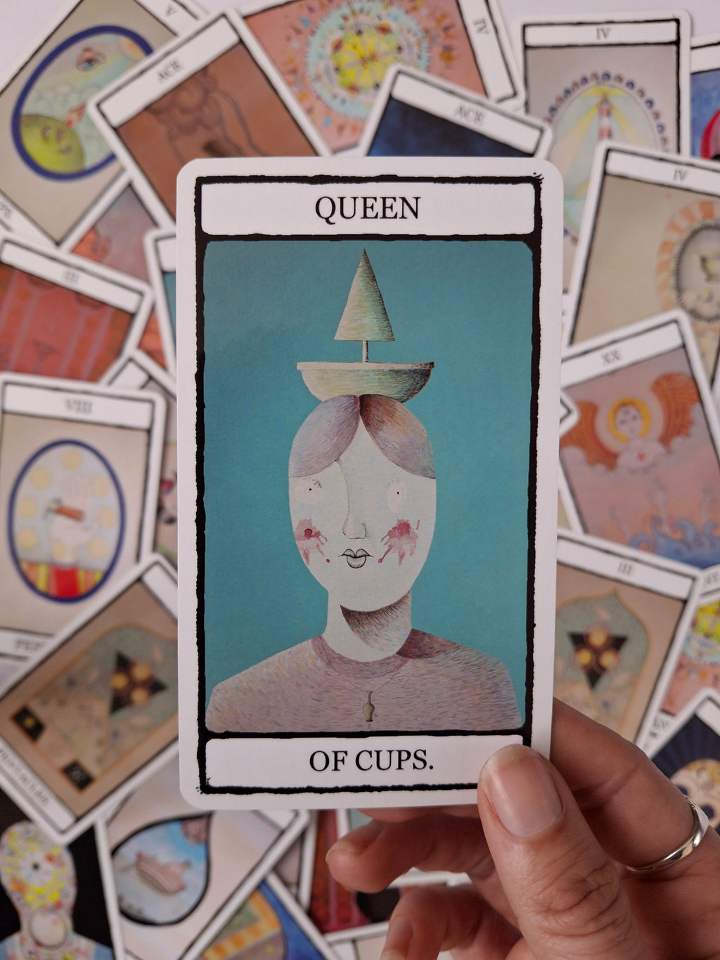 Queen of Cups tarot card featuring original illustration of a woman with a green boat on her head